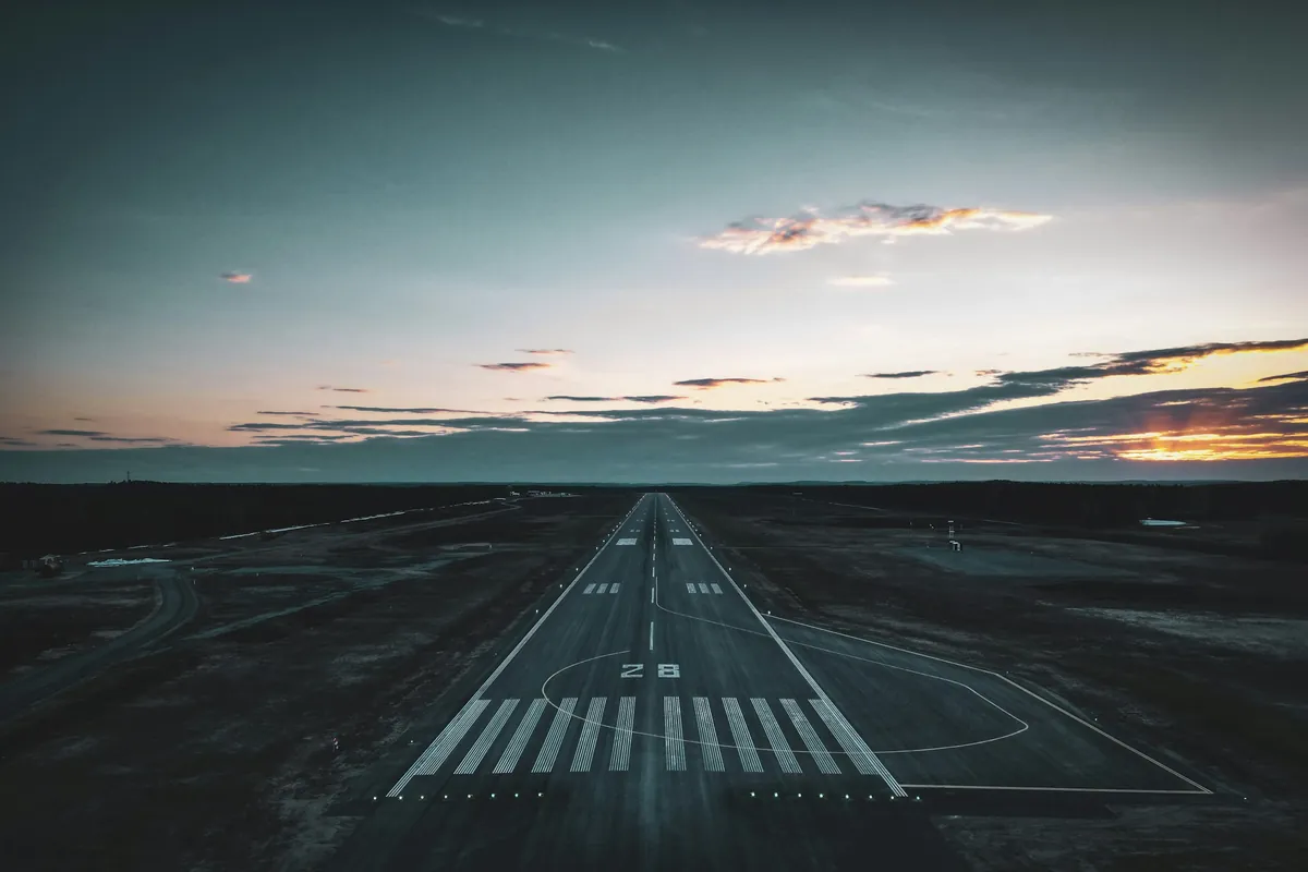 An airport runway from the air at dusk, threshold markings and taxiway lights, no aircraft