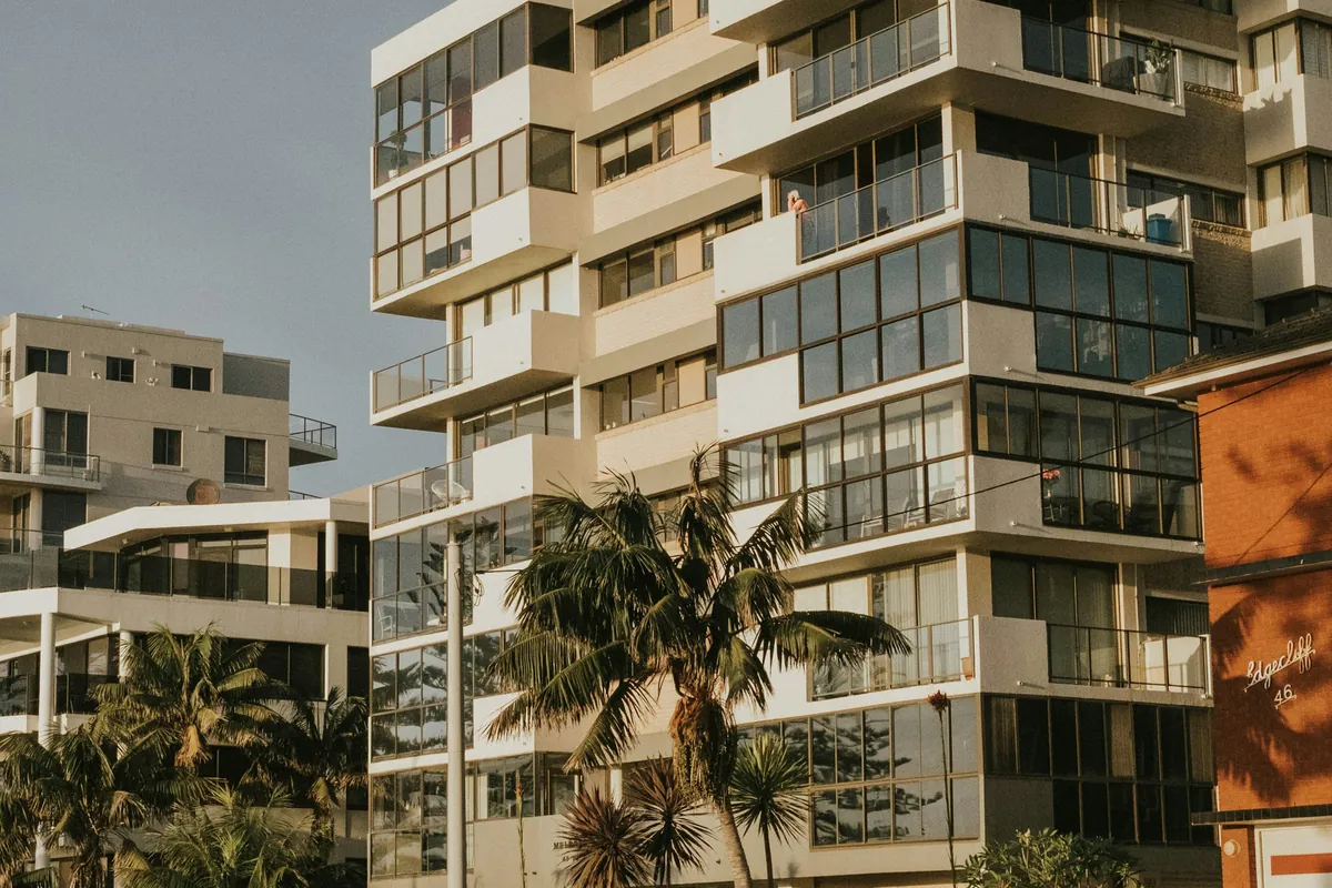 A mid-rise apartment building with glass balconies, palm trees in front, late afternoon light