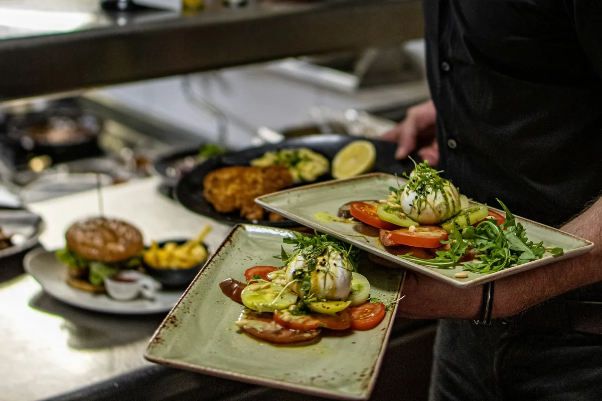 Two plated dishes being carried from the pass of a restaurant kitchen