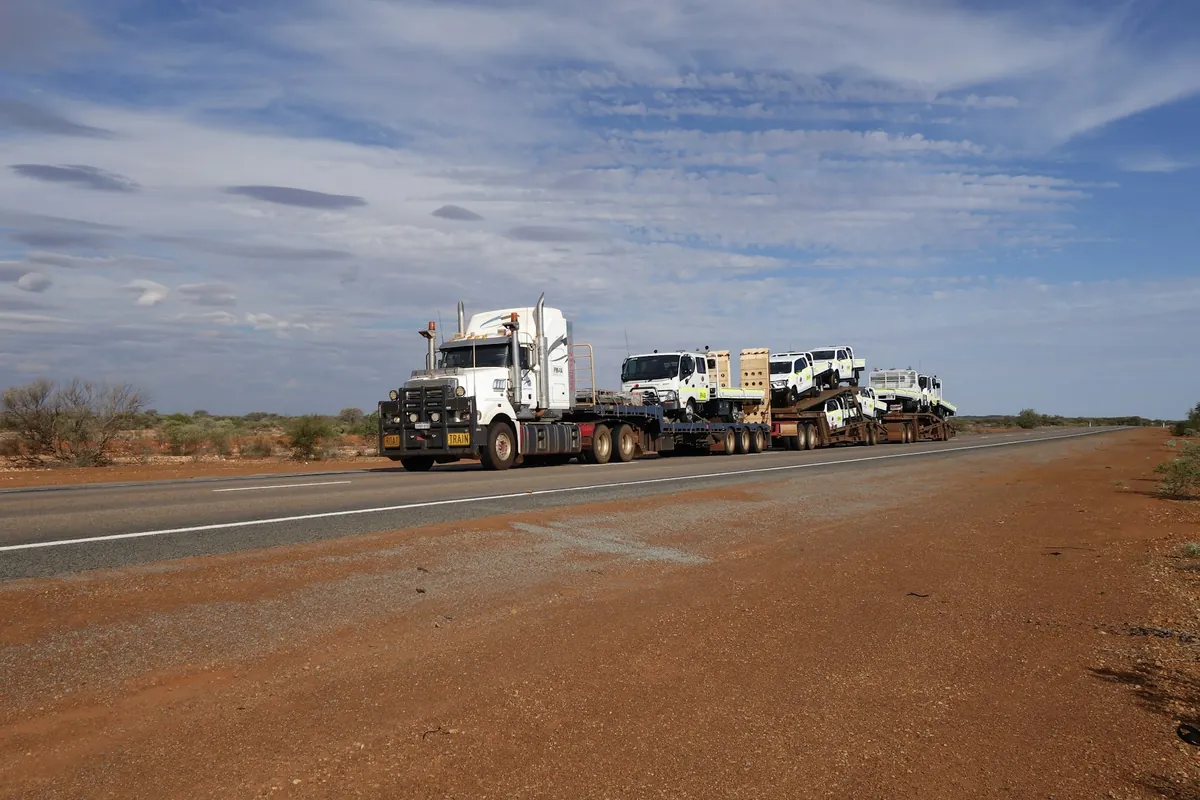 A road train hauling trucks along a red dirt road in Western Australia
